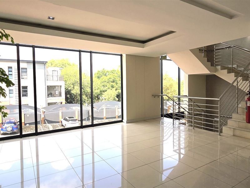 Modern office building entrance lobby featuring polished tile flooring, floor-to-ceiling windows, and a stainless steel staircase.