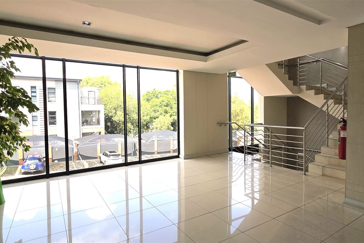 Modern office building entrance lobby featuring polished tile flooring, floor-to-ceiling windows, and a stainless steel staircase.