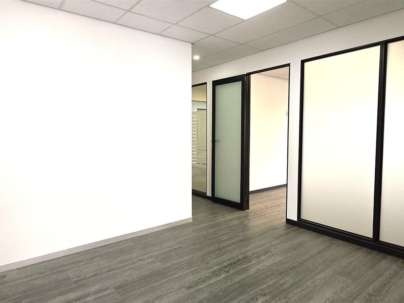 A modern, vacant office space featuring clean white walls, durable laminate flooring, and contemporary frosted glass partitions with black frames.