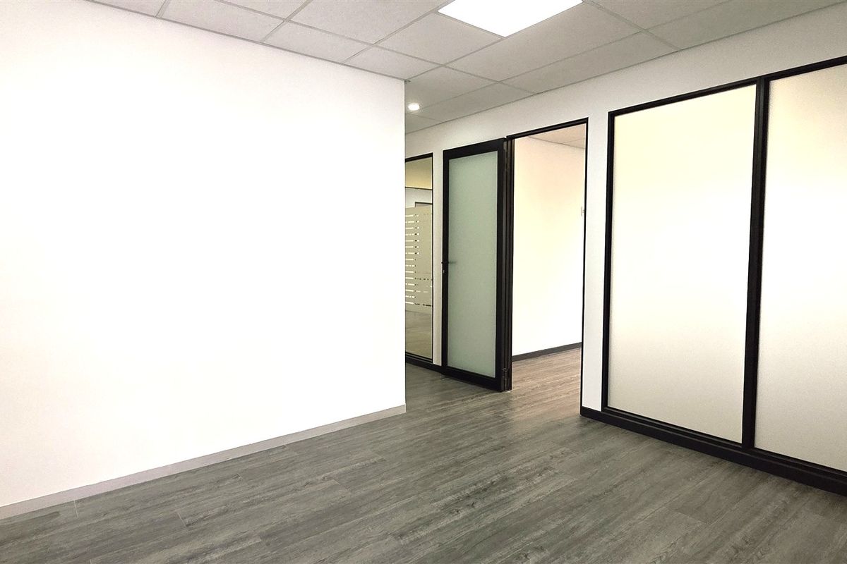 A modern, vacant office space featuring clean white walls, durable laminate flooring, and contemporary frosted glass partitions with black frames.
