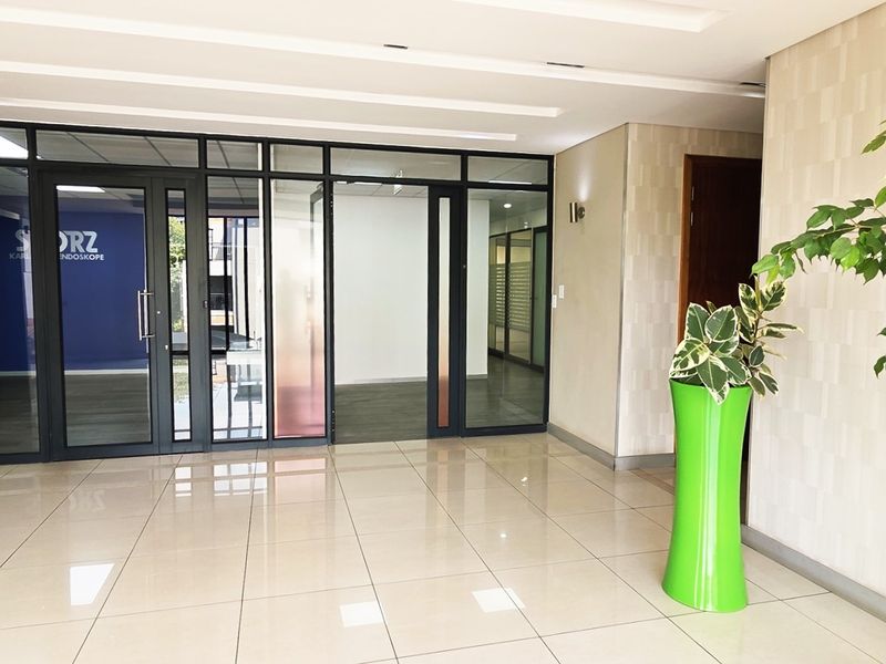Modern office building entrance lobby featuring polished tile flooring, glass partition walls, and recessed ceiling lighting.