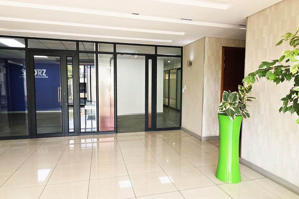 Modern office building entrance lobby featuring polished tile flooring, glass partition walls, and recessed ceiling lighting.