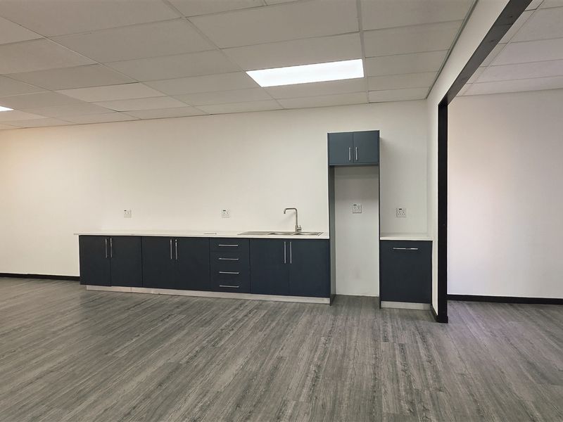 A clean, modern office kitchenette featuring dark blue cabinetry, a stainless steel sink, and wood-look laminate flooring in an open-plan workspace.
