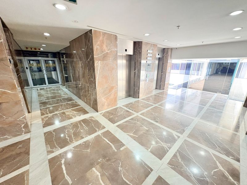 A spacious and modern office building lobby featuring polished marble flooring, marble wall cladding, and dual stainless steel elevator access.