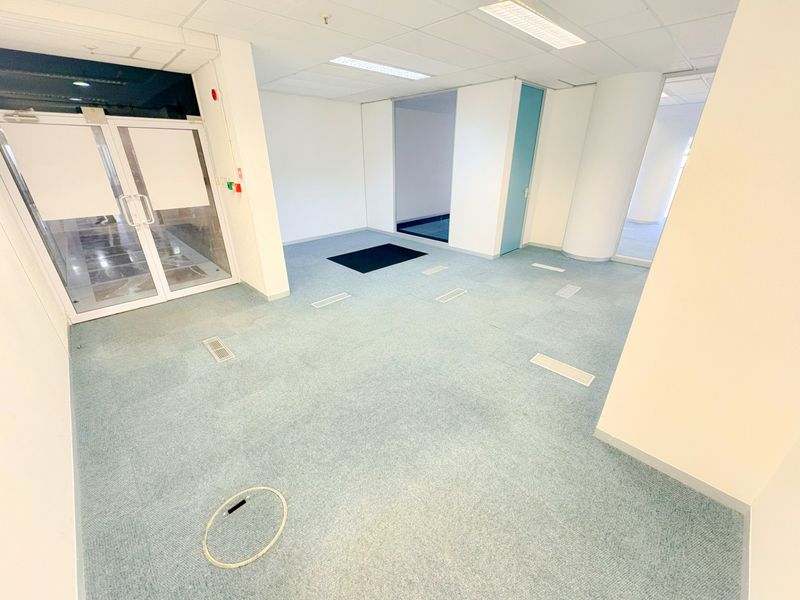 An empty, open-plan office space featuring suspended ceilings, recessed lighting, and carpeted flooring with integrated floor power access points.