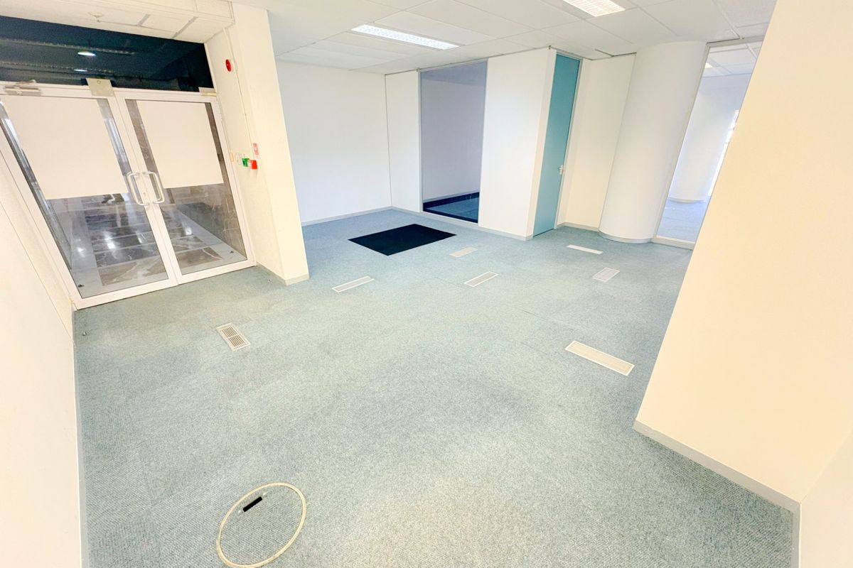 An empty, open-plan office space featuring suspended ceilings, recessed lighting, and carpeted flooring with integrated floor power access points.