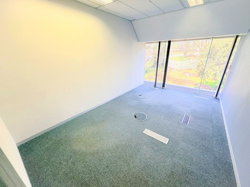 A bright, empty office space featuring carpeted flooring, integrated floor power points, recessed ceiling lighting, and large windows providing natural light.