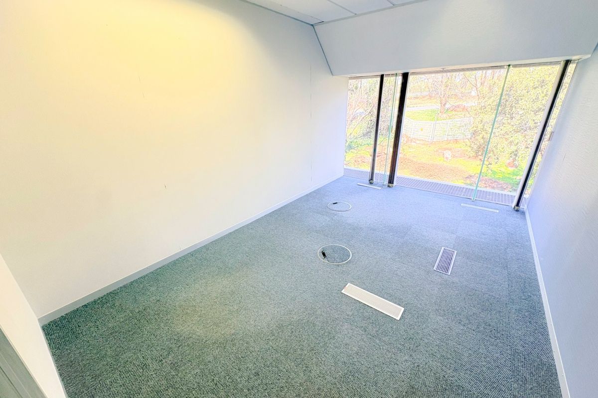 A bright, empty office space featuring carpeted flooring, integrated floor power points, recessed ceiling lighting, and large windows providing natural light.