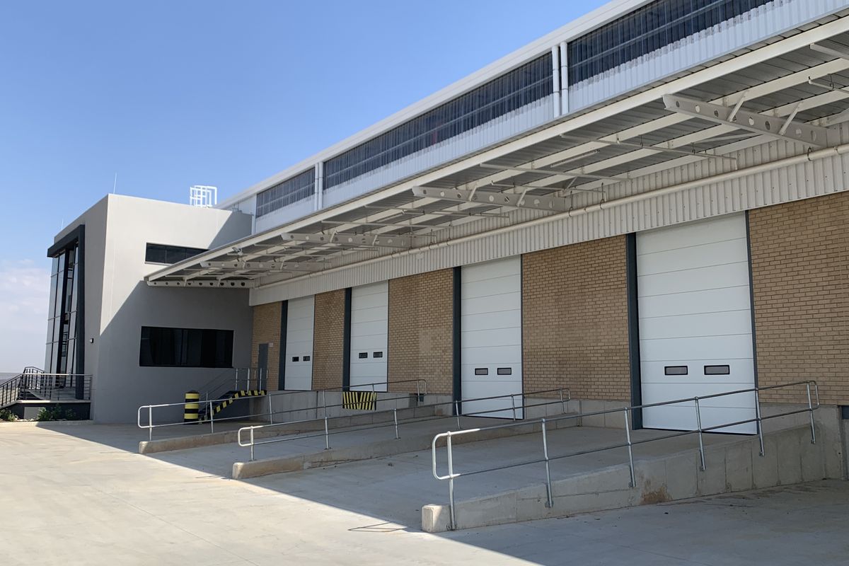 Industrial warehouse exterior featuring multiple loading docks with roller shutter doors, concrete ramps, and a protective steel canopy.