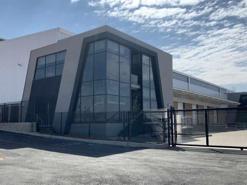 Modern industrial facility featuring contemporary glass facade, metal cladding, secure gated entrance, and functional loading bay area with paved driveway.