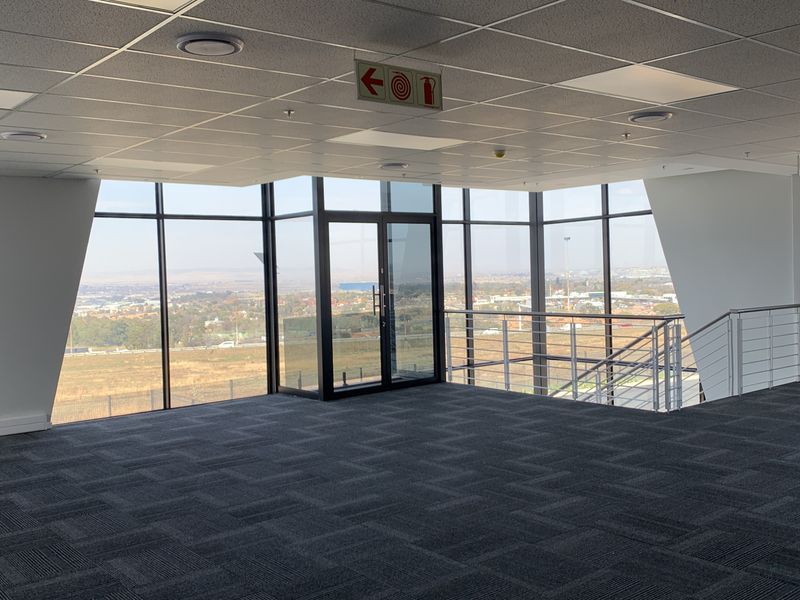 A modern, open-plan office space featuring high-quality carpet tiles, a suspended ceiling, and expansive floor-to-ceiling windows offering panoramic views.