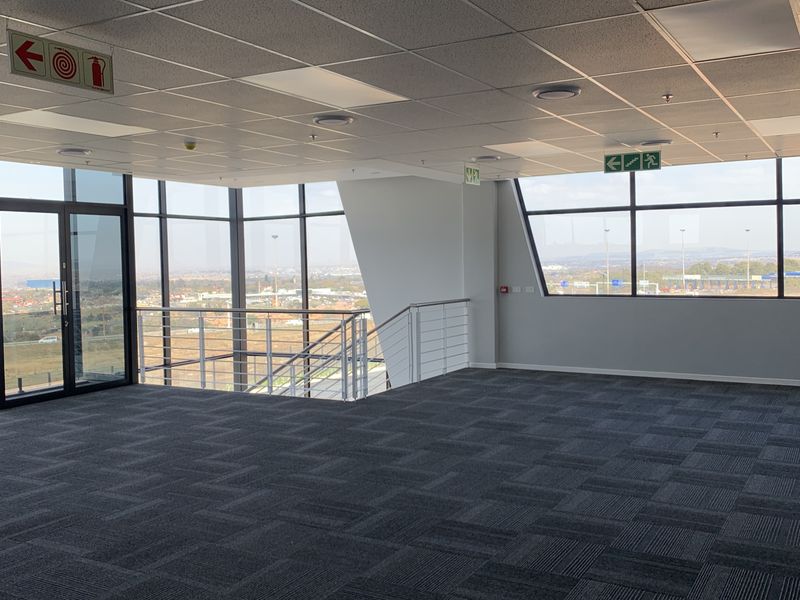 A modern, open-plan office space featuring carpet tiles, a suspended ceiling, and expansive floor-to-ceiling windows offering panoramic views.