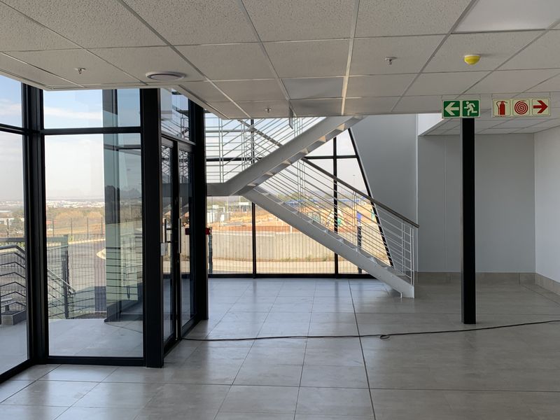 Modern industrial entrance lobby featuring large glass curtain walls, tiled flooring, a sleek metal staircase, and integrated emergency safety signage.