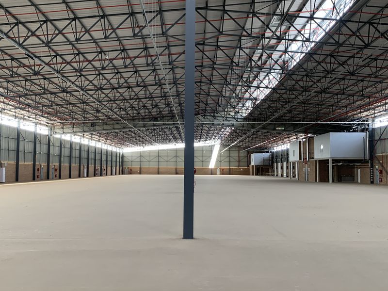Spacious industrial warehouse featuring high ceilings with exposed steel trusses, fire sprinkler system, polished concrete flooring, and large roller shutter access doors.