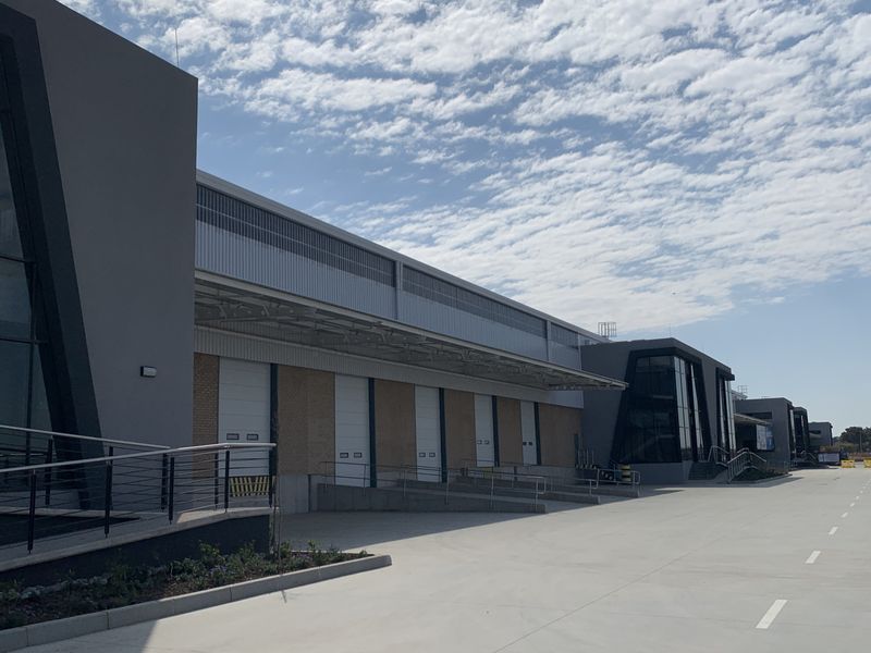 Modern industrial facility featuring multiple loading docks with roller shutter doors, expansive concrete yard, and contemporary glass and metal facade architecture.