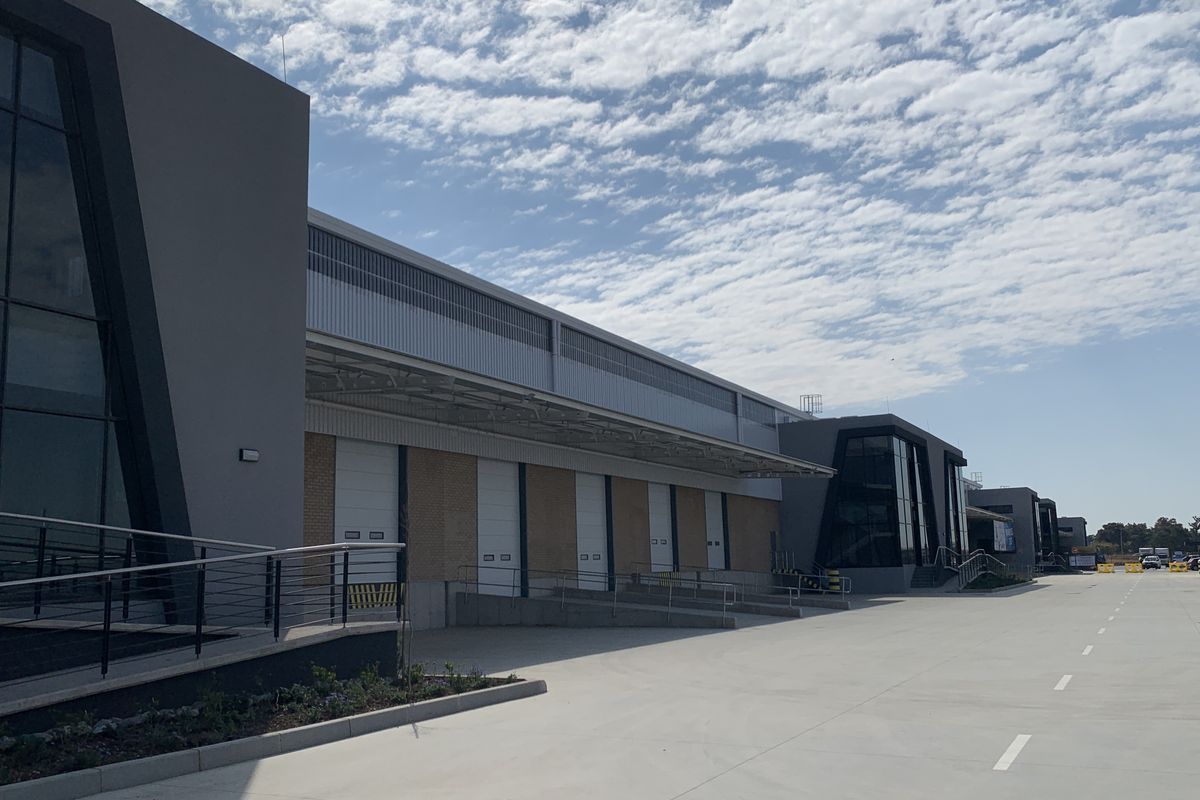Modern industrial facility featuring multiple loading docks with roller shutter doors, expansive concrete yard, and contemporary glass and metal facade architecture.