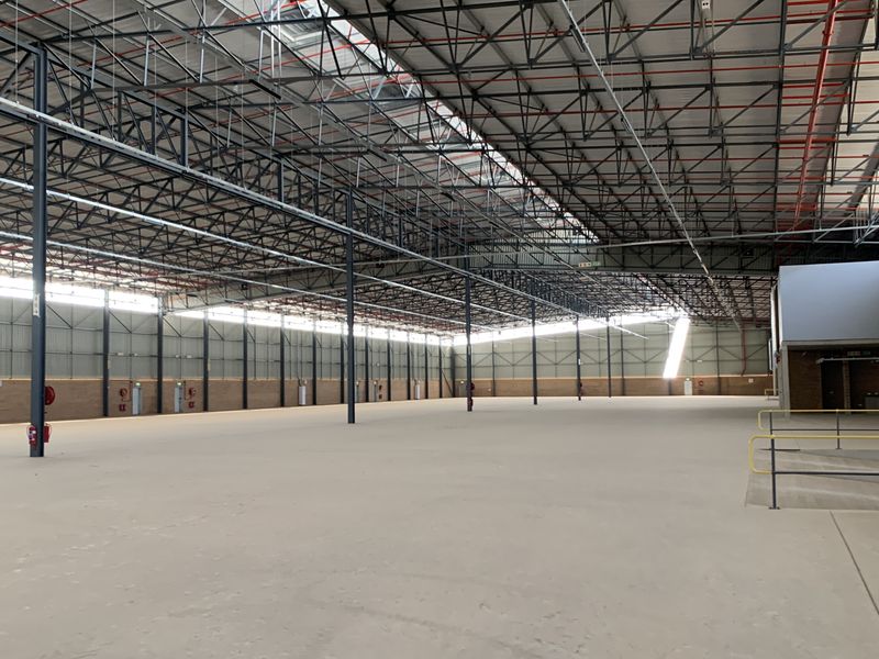 Expansive industrial warehouse space featuring high ceilings with exposed steel trusses, polished concrete flooring, and integrated fire safety systems.
