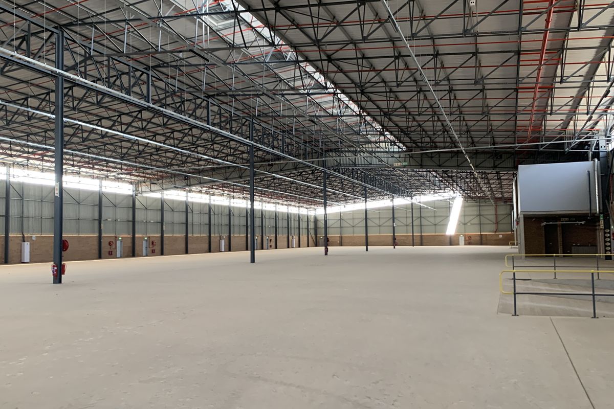 Expansive industrial warehouse space featuring high ceilings with exposed steel trusses, polished concrete flooring, and integrated fire safety systems.