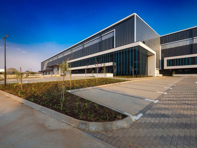 Modern industrial facility featuring metal cladding, paved parking bays, and landscaped garden beds in a well-maintained exterior setting.