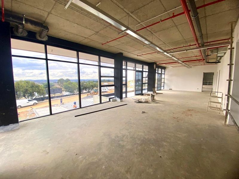 Spacious open-plan industrial unit featuring exposed concrete ceilings, fire sprinkler systems, and expansive floor-to-ceiling windows offering natural light and exterior views.
