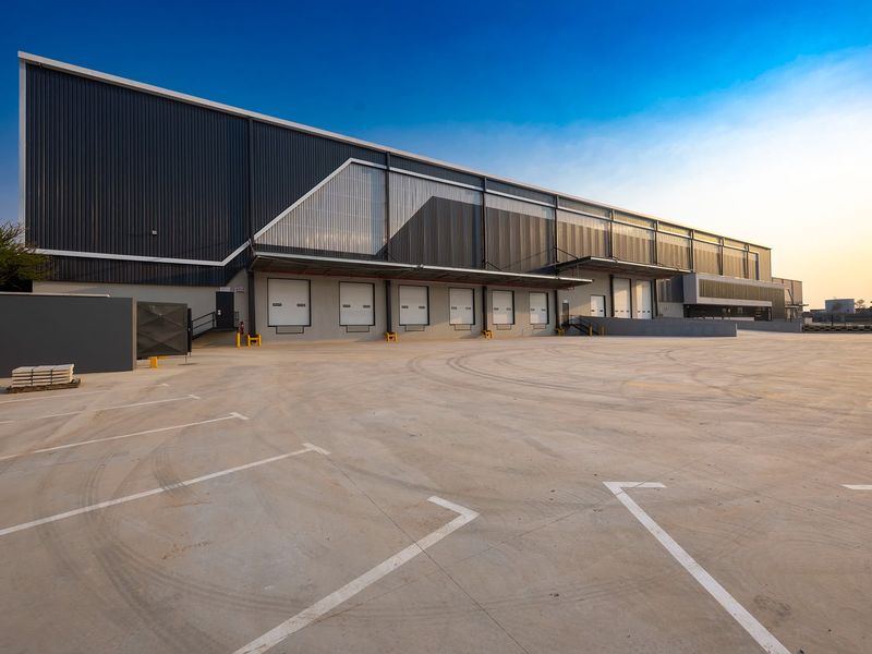 Modern industrial warehouse facility featuring multiple loading docks, roller shutter doors, and a spacious concrete yard area for logistics and distribution operations.