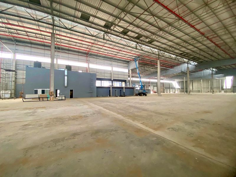 Large industrial warehouse space featuring high ceilings with exposed steel trusses, fire sprinkler systems, and expansive concrete flooring suitable for logistics or manufacturing operations.