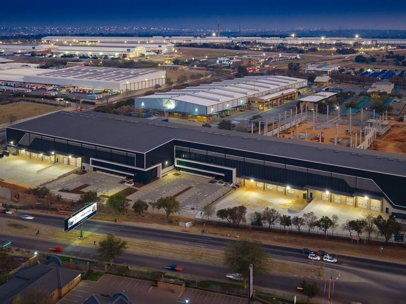 Aerial view of a modern industrial warehouse complex featuring extensive loading bays, paved parking, and secure perimeter fencing in a commercial business park.