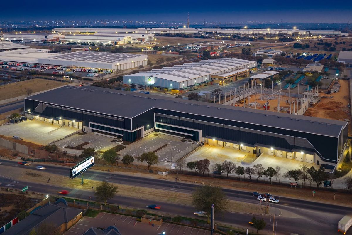 Aerial view of a modern industrial warehouse complex featuring extensive loading bays, paved parking, and secure perimeter fencing in a commercial business park.