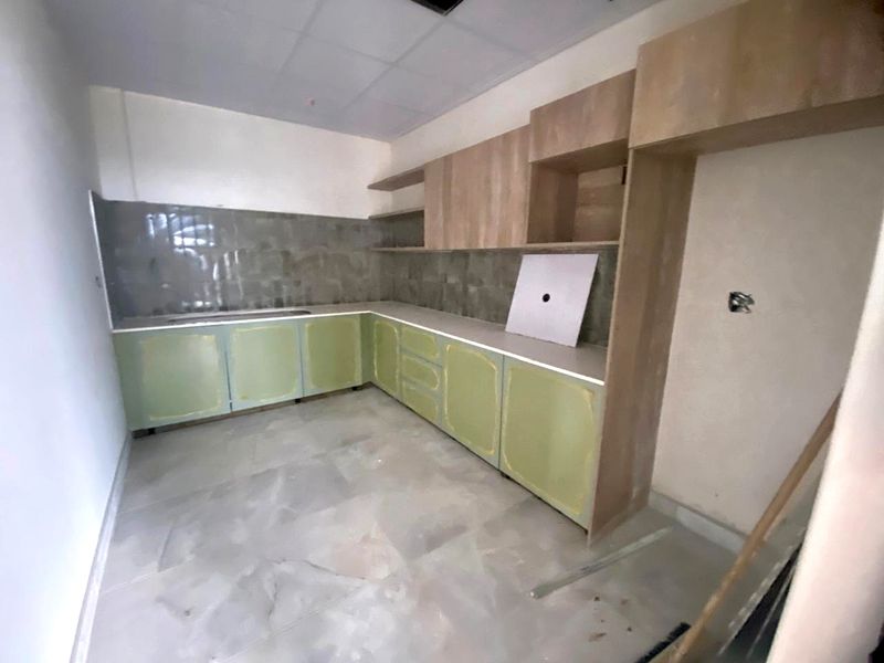 An unfinished kitchen area featuring light green base cabinetry, wood-tone upper shelving, tiled backsplash, and a drop-in sink, awaiting final installation and finishing touches.