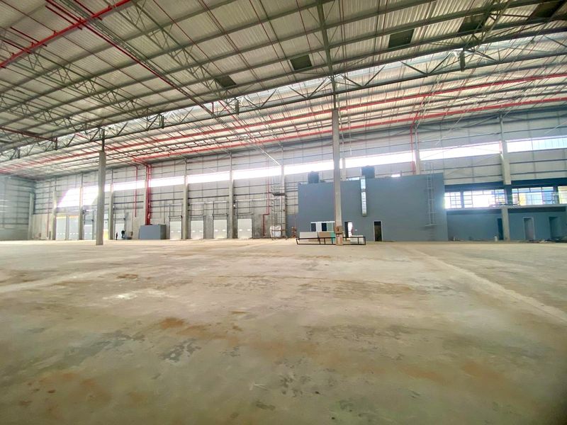 Spacious industrial warehouse featuring high ceilings with exposed steel trusses, fire sprinkler system, concrete flooring, and multiple loading bay doors.