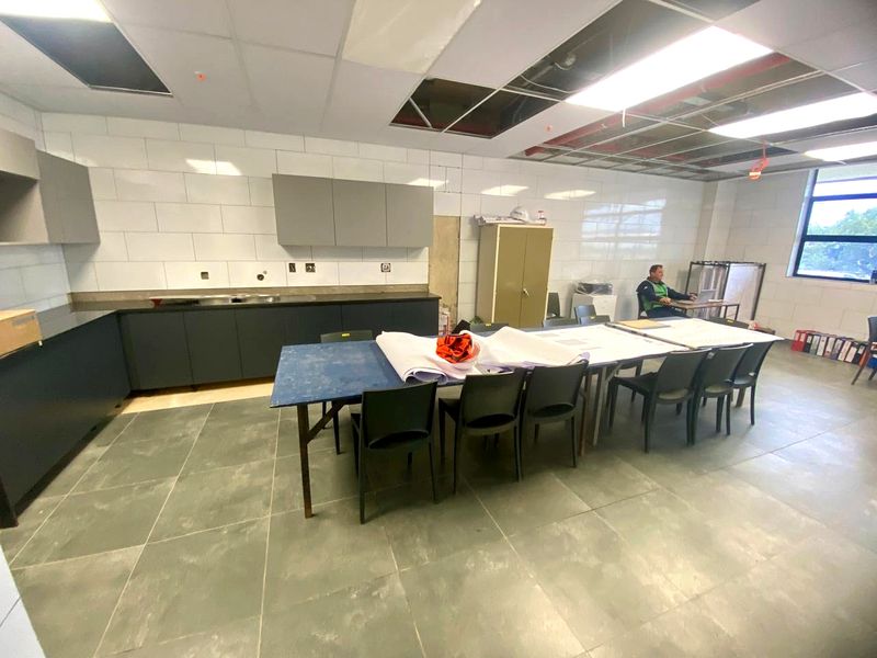 Industrial kitchen area featuring dark cabinetry, tiled splashbacks, and tiled flooring, currently undergoing ceiling maintenance with exposed infrastructure.