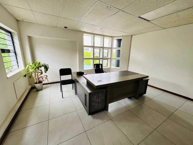 A functional office space featuring tiled flooring, a suspended ceiling, and large grid-style windows providing natural light.