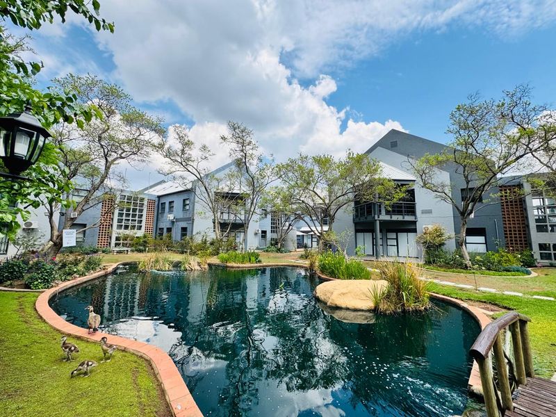 A well-maintained office park exterior featuring a central ornamental pond, landscaped gardens, and modern multi-story office buildings with balconies.
