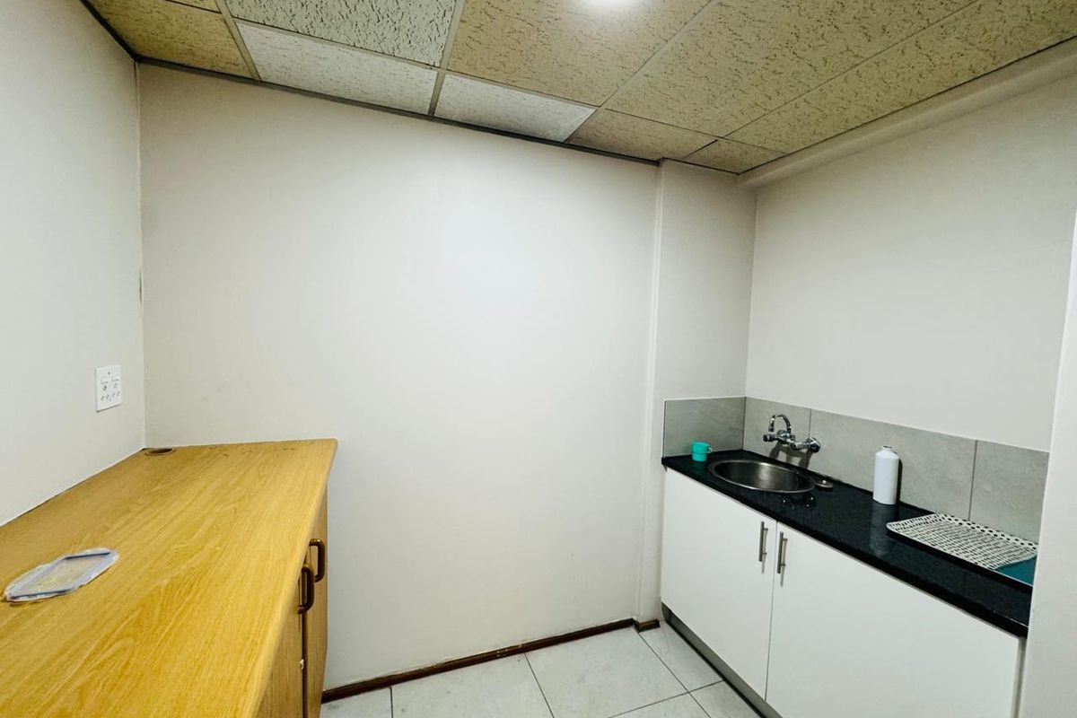 A compact office kitchenette featuring built-in cabinetry, a sink, and tiled flooring, providing essential utility space for a professional environment.