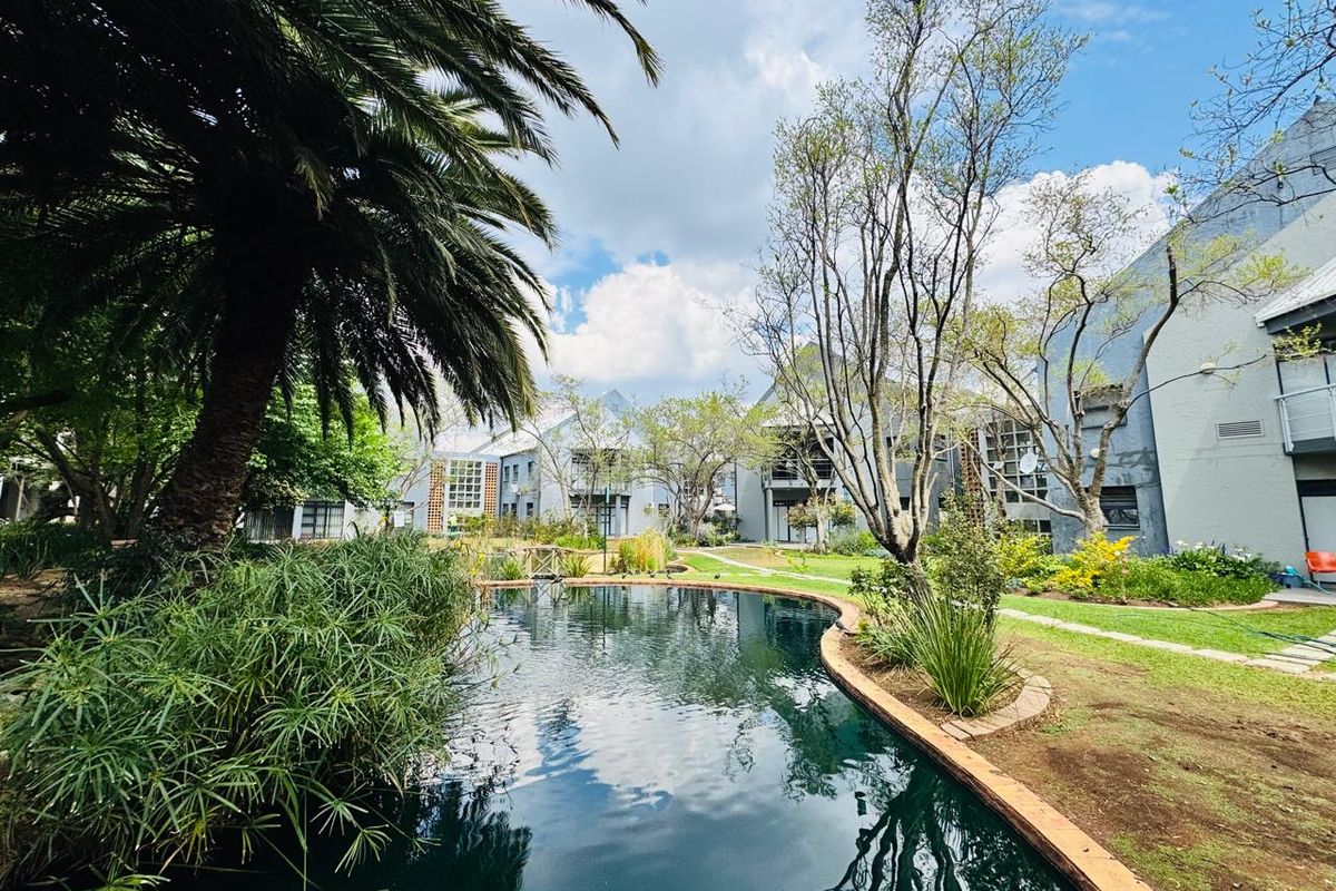 A tranquil outdoor office complex featuring a landscaped garden with a central swimming pool and mature trees surrounding the building exterior.