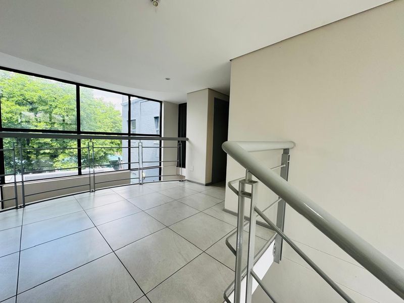 A bright, modern landing or hallway area featuring large windows, tiled flooring, and a sleek metal balustrade overlooking the staircase.