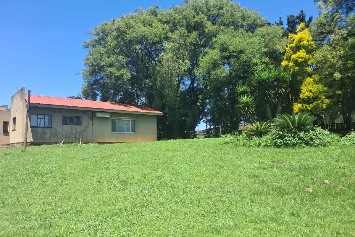 A view of the side elevation of the dwelling set on a large, grassy small holding plot with mature trees and established garden.