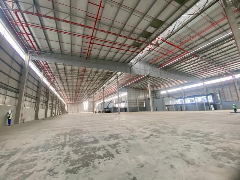 A large, open-plan industrial warehouse space featuring high ceilings with exposed steel trusses, fire sprinkler systems, and durable concrete flooring.