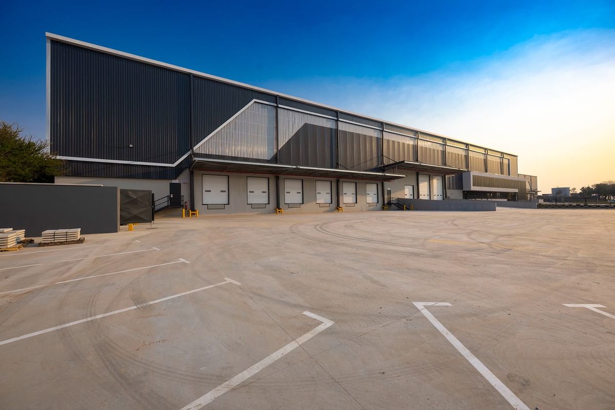Modern industrial warehouse facility featuring multiple loading docks, roller shutter doors, and a spacious concrete yard area for logistics and distribution operations.