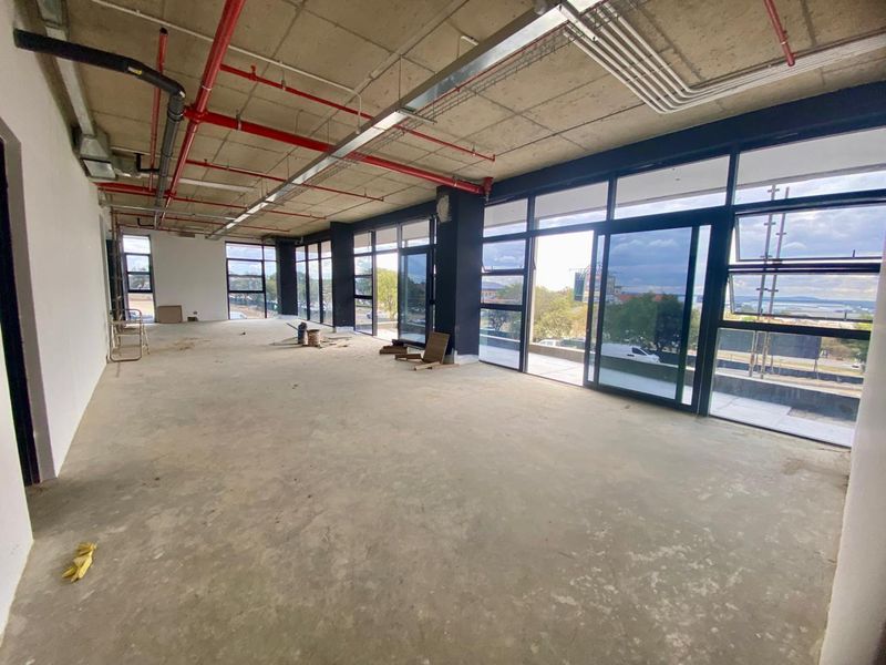 Spacious open-plan industrial unit featuring exposed ceilings, fire sprinkler systems, and expansive floor-to-ceiling windows providing ample natural light.