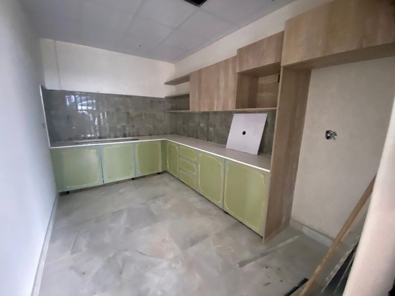 An unfinished kitchen area featuring light green base cabinetry, wood-tone upper cabinets, tiled backsplash, and neutral floor tiles, currently awaiting final installation and hardware.