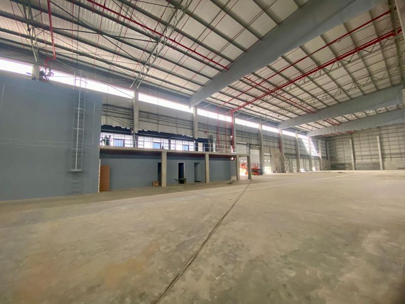 Spacious industrial warehouse featuring high ceilings, exposed steel roof structure, integrated fire sprinkler system, and a mezzanine level with concrete flooring.