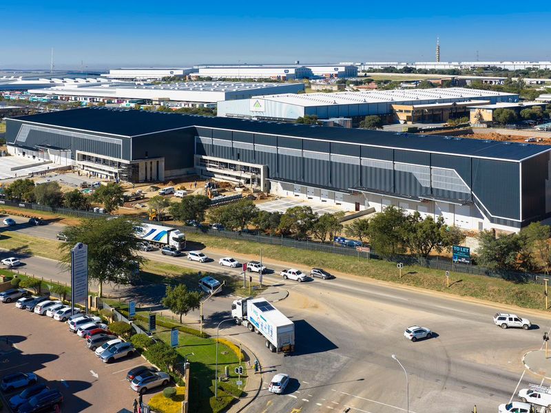 Aerial view of a large-scale industrial warehouse facility featuring extensive metal cladding, loading bays, and surrounding infrastructure under development.