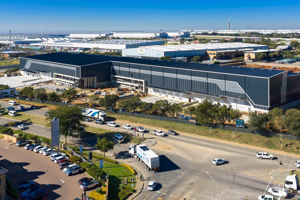 Aerial view of a large-scale industrial warehouse facility featuring extensive metal cladding, loading bays, and surrounding infrastructure under development.