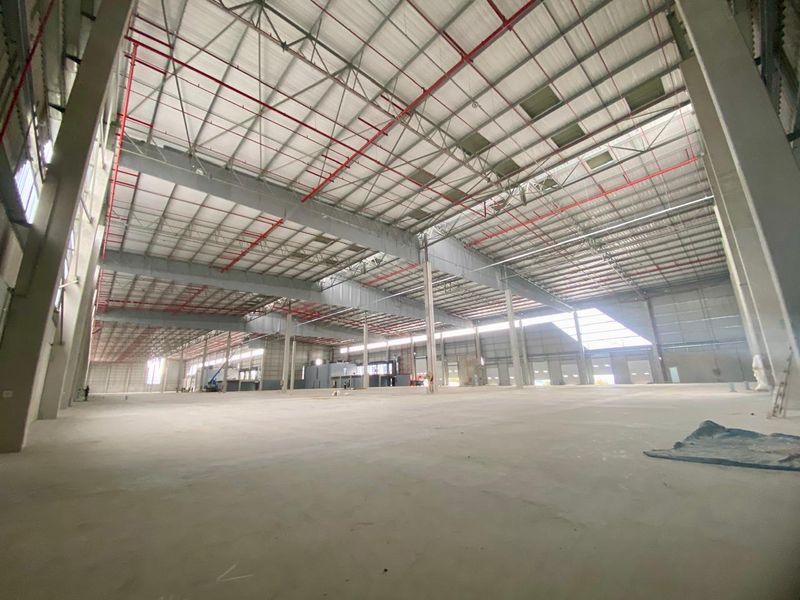 Expansive industrial warehouse space featuring high ceilings, exposed steel structural framing, integrated fire sprinkler systems, and polished concrete flooring.