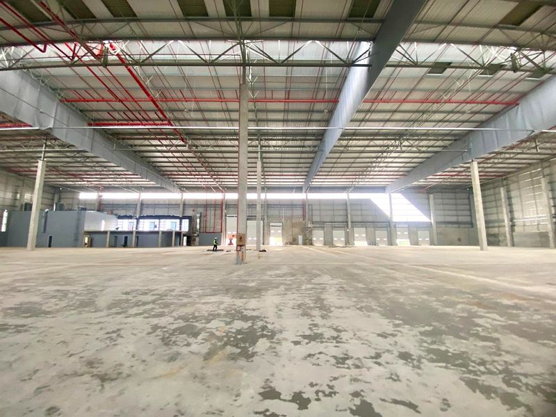Expansive industrial warehouse space featuring high ceilings with exposed steel trusses, fire sprinkler systems, and multiple roller shutter doors.