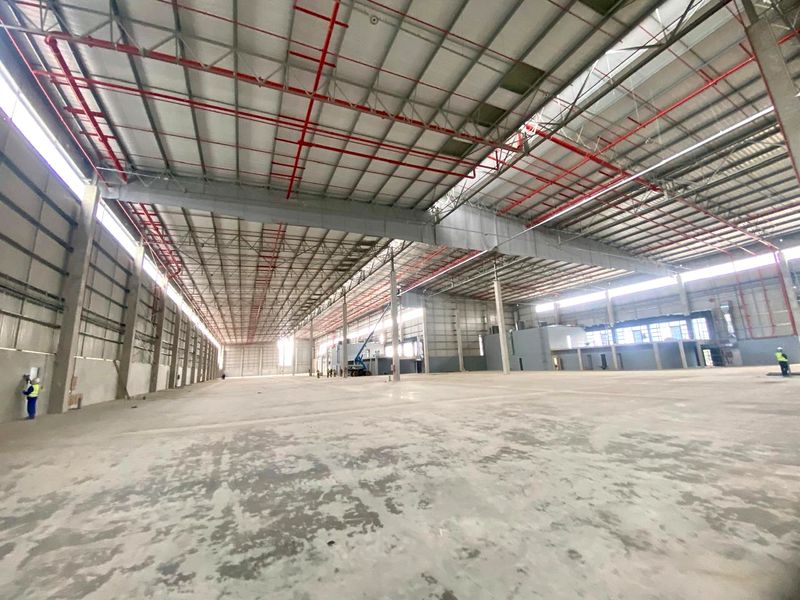 Expansive industrial warehouse space featuring high ceilings with exposed steel trusses, fire sprinkler systems, and durable concrete flooring.