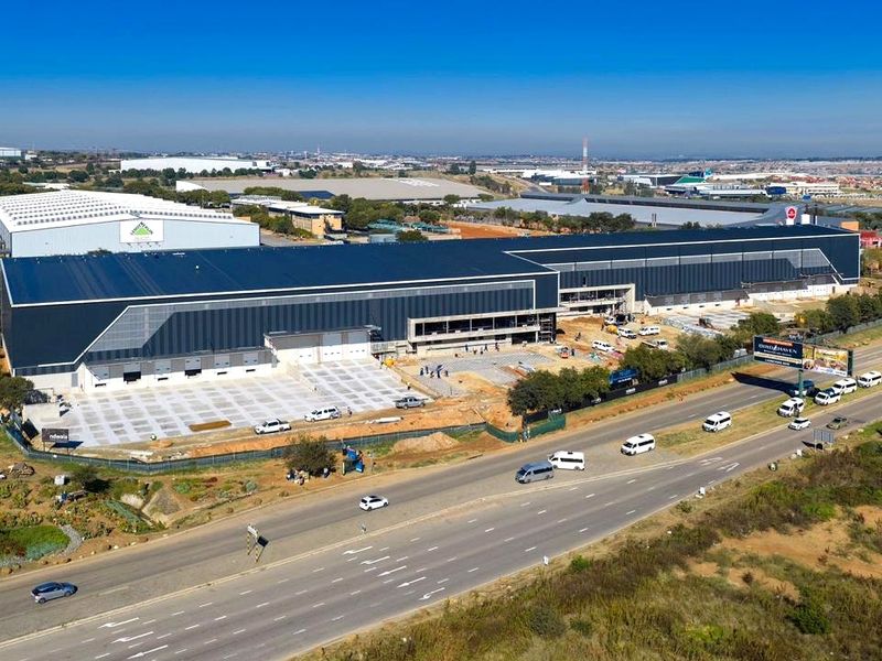 Aerial view of a large industrial warehouse facility under construction, featuring extensive metal roofing, loading bays, and a concrete yard area.