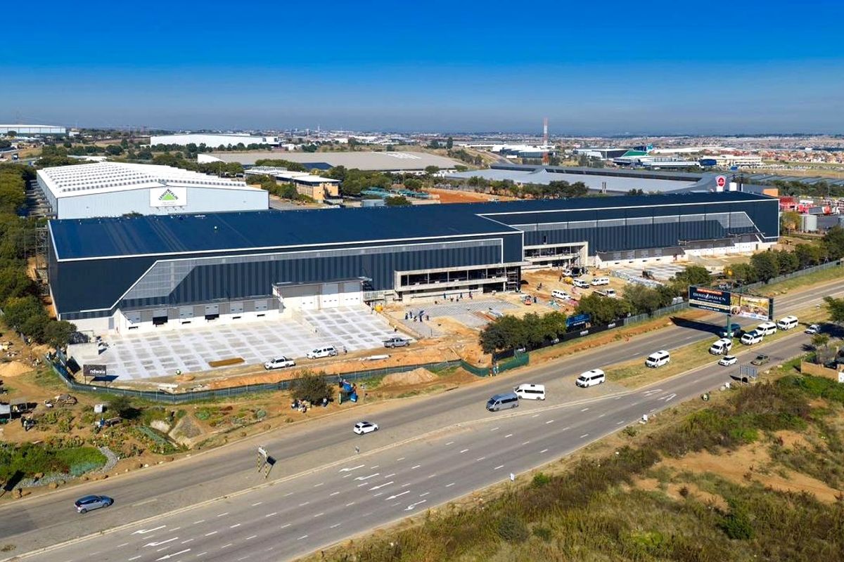 Aerial view of a large industrial warehouse facility under construction, featuring extensive metal roofing, loading bays, and a concrete yard area.