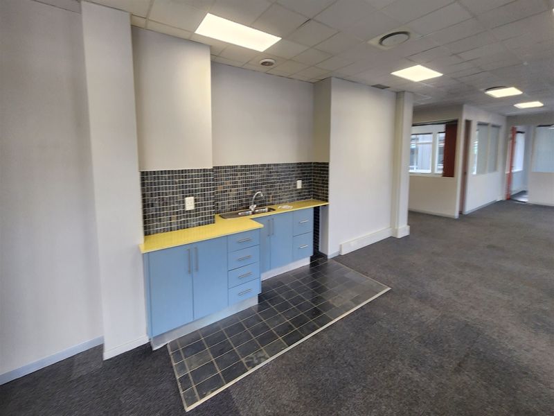 A functional office kitchenette featuring built-in blue cabinetry, a stainless steel sink, and a tiled backsplash, set within an open-plan office environment.